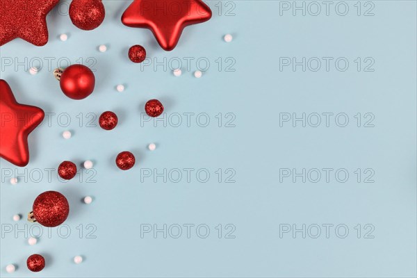 Red Christmas tree baubles in shape of balls and stars and white snowball ornaments in corner of light blue background with empty copy space