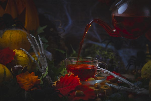 Pouring tea into glass cup surrounded by Halloween decorations