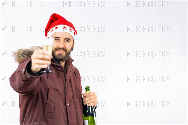 Young very happy Caucasian man with red Christmas hat toasting with a glass of champagne on a white background