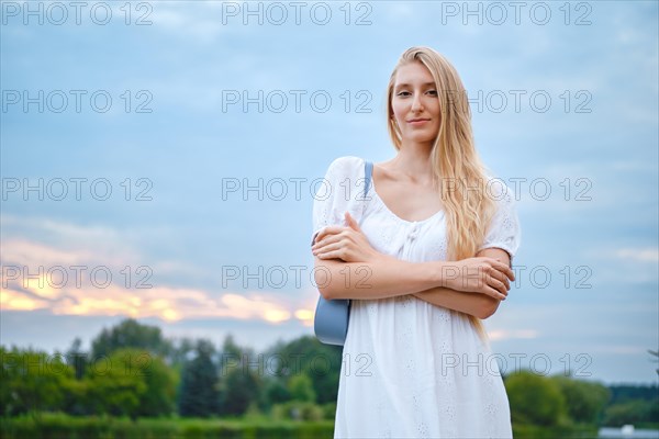 Portrait of a woman with crossed arms by the river with evening sky on background
