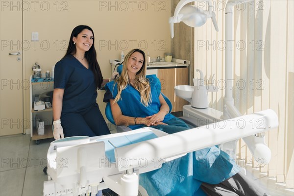 Beautiful young female patient sitting in dentist chair. Patient and dentist look and smile at camera