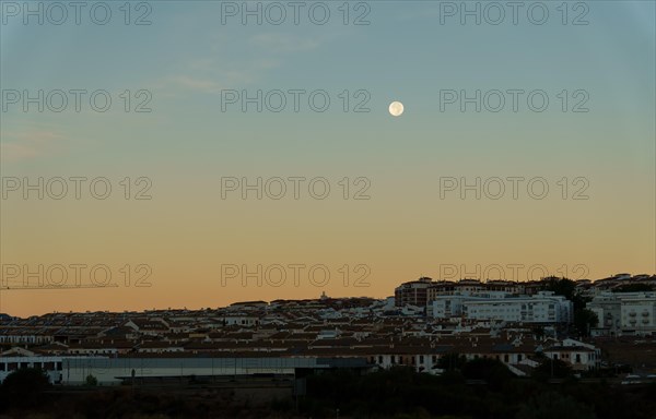 Sunrise cityscape with reddish and blue tones with a full moon in the sky in ronda
