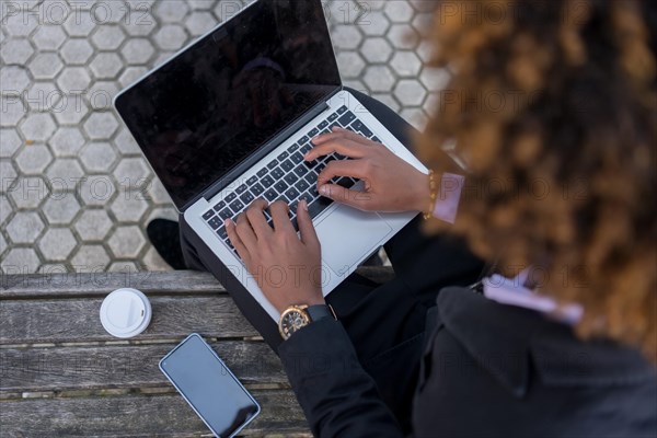 Top view of an unrecognizable businessman using laptop sitting on a bench next to a coffee cup and a mobile phone