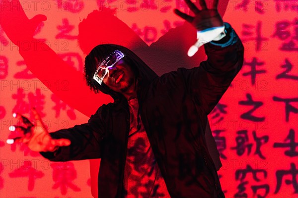 Studio portrait with red neon lights of a cool man with augmented reality goggles dancing