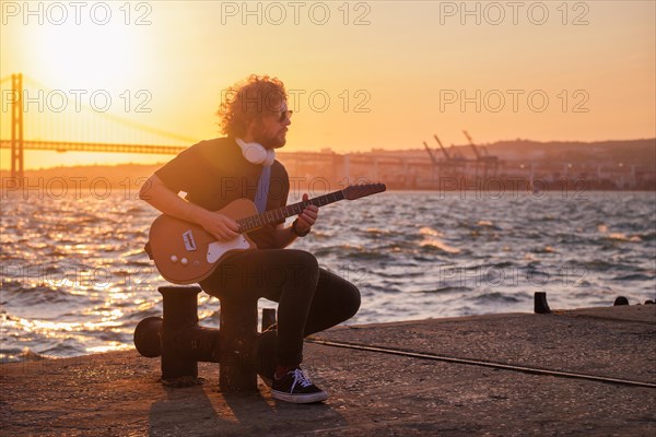 Hipster street musician in black playing electric guitar in the street on sunset