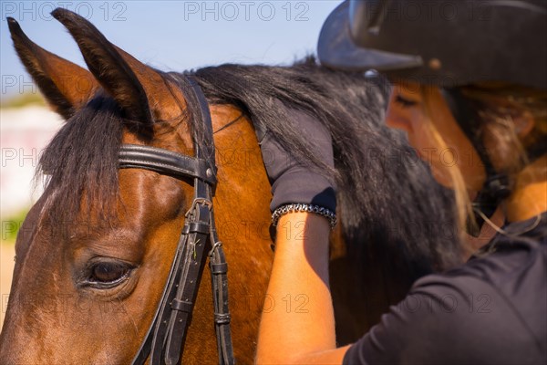 Caucasian blonde girl on horseback stroking a brown horse