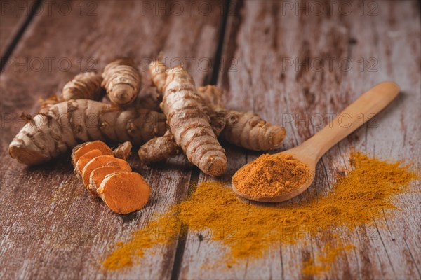 Fresh turmeric root and ground turmeric in a wooden spoon poured out on a wooden table