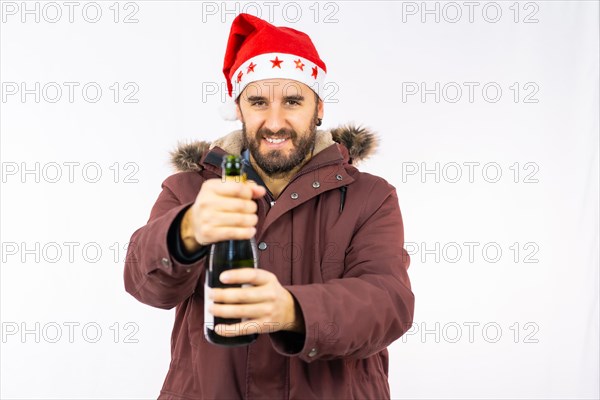 Young very happy Caucasian man with red Christmas hat opening a bottle of champagne on a white background