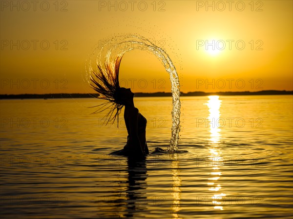 Young woman in the water throws back her long hair with a surge of water