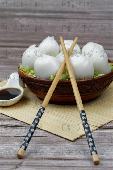 Xiao long bao of prawns on a bed of lettuce in a wooden bowl with chopsticks and a ceramic spoon with soy sauce