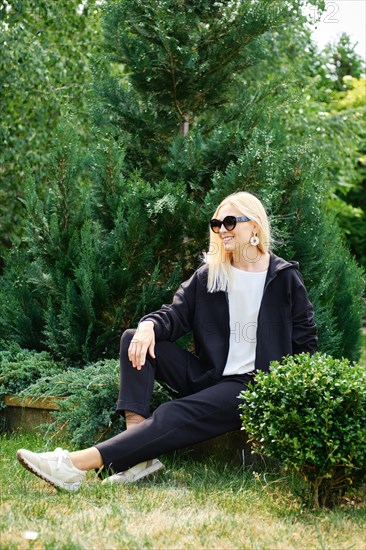 Blonde woman in fleece tracksuit sits in profile in the garden