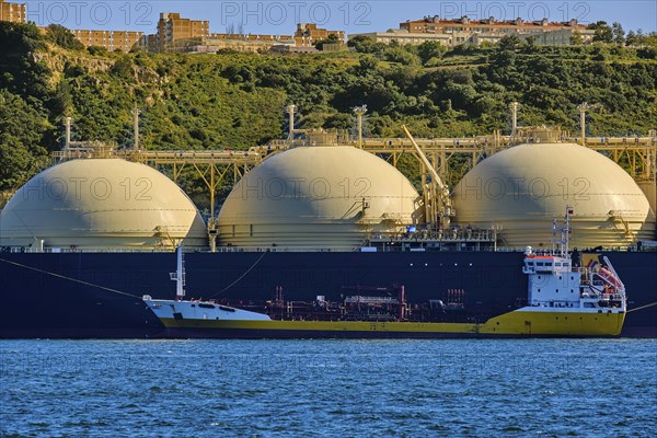 LNG or liquified natural gas tanker moored by industrial pier and green hill on sunny day. Alternative gas supply