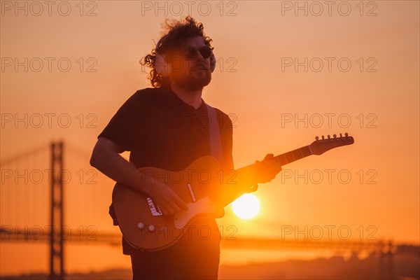 Hipster street musician in black playing electric guitar in street outdoors on sunset