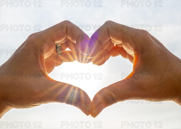 Woman Hands Making a Heart Shape Against the Sky with Sun and Sunbeam in Switzerland