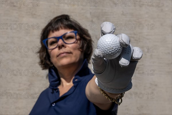 Female Golfer with Eyeglasses and a Glove Holding Up Her Golf Ball and Looking at Camera in a Sunny Day in Switzerland