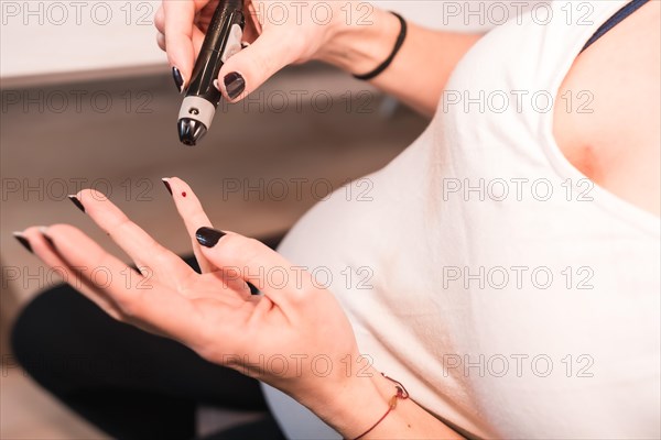 Young pregnant brunette performing a gestational diabetes self-test to control sugar. Bleeding blood from his finger with a prick