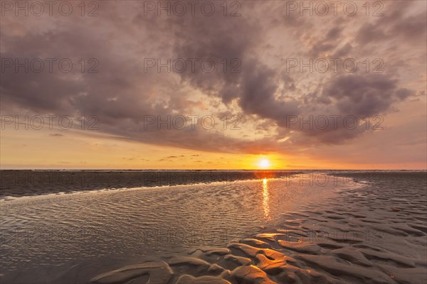Seascape showing beach at low tide and sunset with cloudy sky over the Wadden Sea