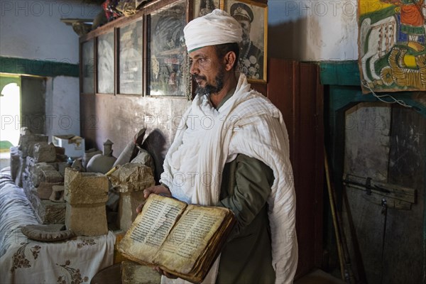 Orthodox priest showing 14th century bible inside the Temple of Yeha