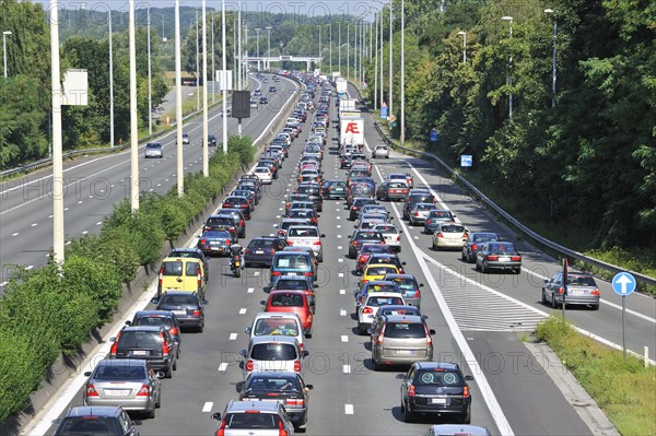 Cars and trucks queueing in highway lanes at approach slip road during traffic jam on motorway during summer holidays