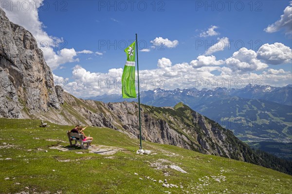 Young couple sitting on bench next to green flag of the Austrian Alpine Club