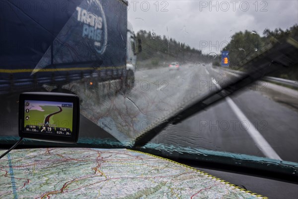 Speeding truck overtaking car on highway during heavy rain shower seen from inside of vehicle with GPS and road map on dashboard