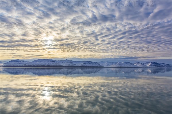 Snow covered mountains at Billefjorden at sunset and clouds reflected in the Arctic sea