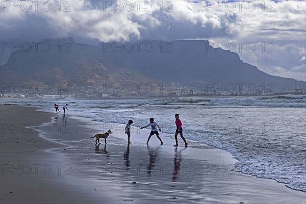 Rain clouds over Table Mountain and children playing on sandy Sunset Beach near Cape Town
