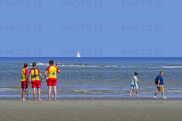 Three young Belgian lifeguards watching over empty sea along the North Sea coast in summer at Koksijde