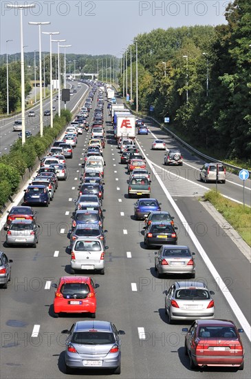 Cars and trucks queueing in highway lanes at approach slip road during traffic jam on motorway during summer holidays