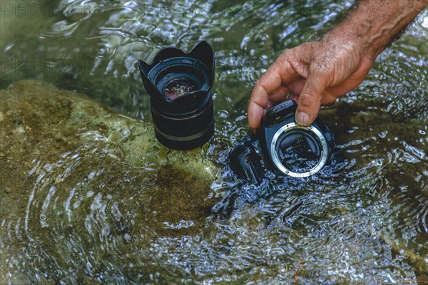 A man cleans the sensor of his reflex camera in the water of a river by flooding it from the inside