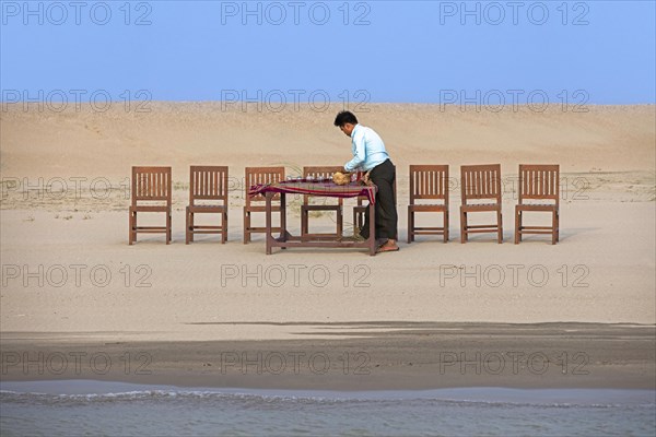 Burmese servant preparing dinner and setting the table for tourists at sunset along the Irrawaddy River