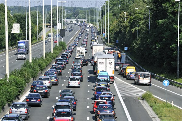 Cars and trucks queueing in highway lanes at approach slip road during traffic jam on motorway during summer holidays