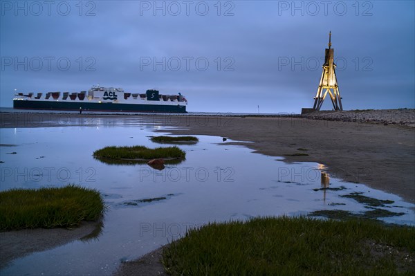 Kugelbake illuminated with cargo ship at dusk