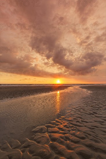 Seascape showing beach at low tide and sunset with cloudy sky over the Wadden Sea