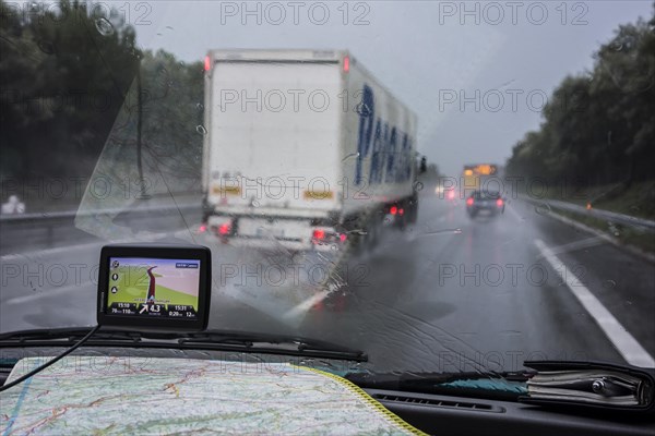 Speeding truck overtaking cars on highway during heavy rain shower seen from inside of vehicle with GPS and road map on dashboard