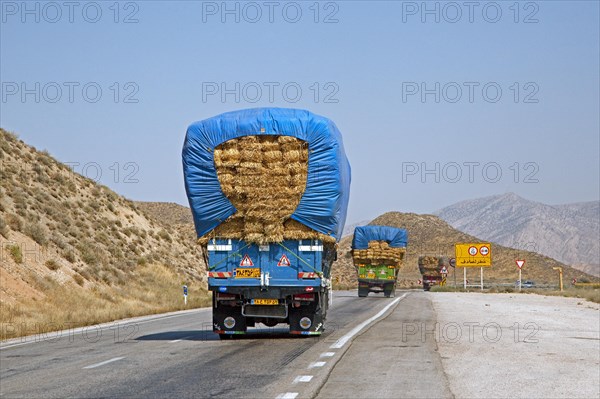 Convoy of heavily loaded trucks transporting bales of hay over highway in Iran