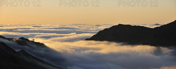 View over silhouetted chairlifts and mountains covered in mist at sunrise seen from the Col du Tourmalet