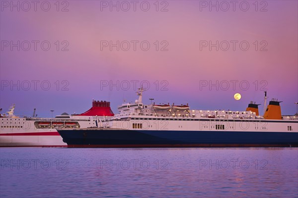 Two ferries moored parallel by pier at colorful sunset during moonrise. Popular transportation for island hopping in Mediterranean sea