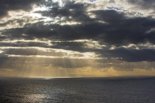 Sunrays bursting through dense sheet of rain clouds over sea water at sunset