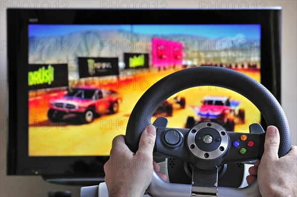 Steering wheel controller in front of television screen showing cars in racing game