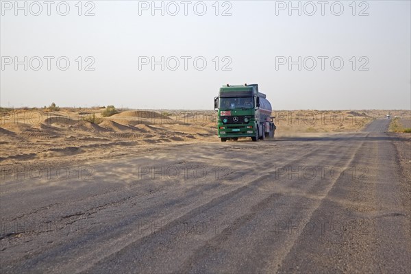 Truck crossing the Karakum desert in Turkmenistan and wind blowing sand from the dunes over the road