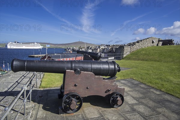 Cannon at 17th century Fort Charlotte in the centre of Lerwick and cruise ship in the Bressay Sound