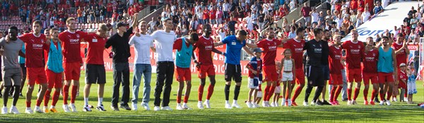 The 1.FC Heidenheim team celebrates the victory under the fan curve
