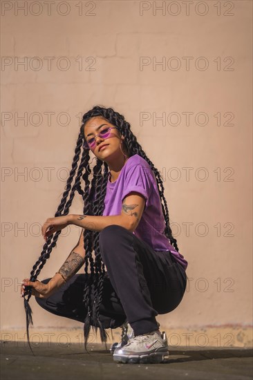 Urban session. A young dark-skinned woman with long braids and purple glasses