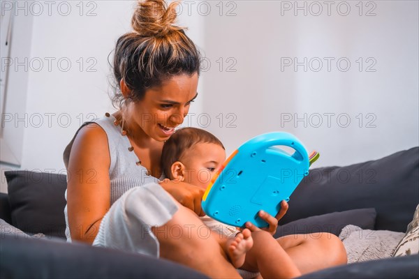 Young Caucasian mother with her son sitting on the black sofa in their home. Teleworking and caring for your child