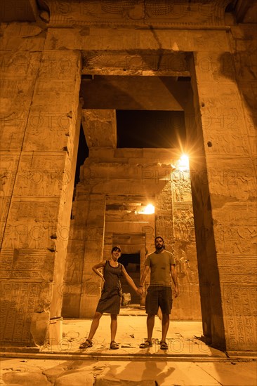 A couple of tourists between the columns at night of the temple of Kom Ombo in traditional dress