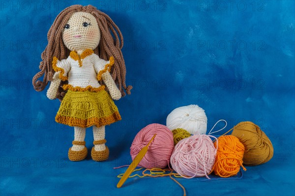 Amigurumi doll handmade on a blue background with the yarns used for its elaboration