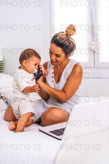 Young Caucasian mother with her son in the room on top of the bed. Mother teleworking and caring for her child