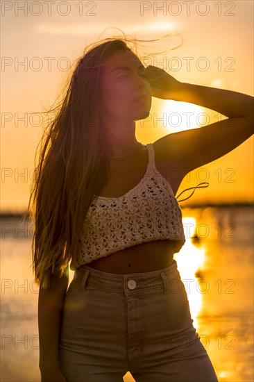 Summer lifestyle. A young blonde Caucasian woman in a white short wool sweater on a beach sunset