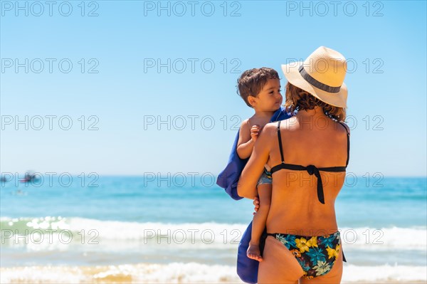 Mother with hat with her son embraced by the sea